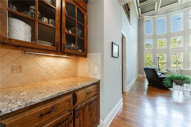 652 Pathview Ct, Dacula, GA 30019 - kitchen featuring light wood-style flooring, light stone counters, glass insert cabinets, a towering ceiling, and tasteful backsplash