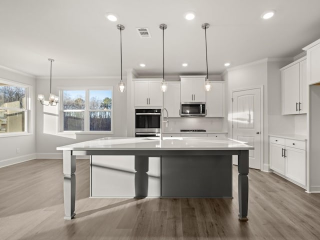 kitchen with a center island with sink, hanging light fixtures, appliances with stainless steel finishes, a kitchen breakfast bar, and white cabinets