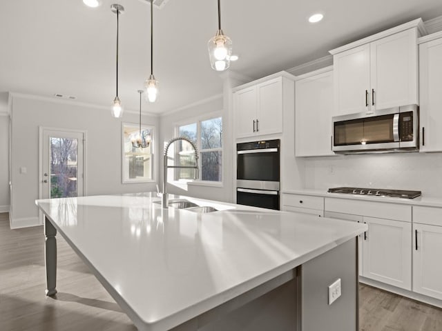 kitchen with white cabinetry, stainless steel appliances, an island with sink, and hanging light fixtures