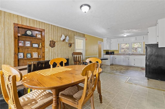 dining space featuring wooden walls, crown molding, a textured ceiling, and sink