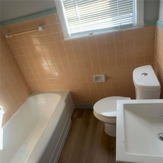 bathroom with a wealth of natural light, a tub, tile walls, and wood finished floors