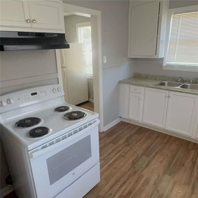 kitchen featuring white appliances, white cabinets, light countertops, under cabinet range hood, and a sink