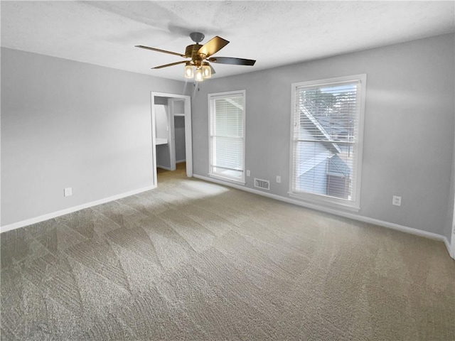 carpeted spare room featuring a textured ceiling, baseboards, visible vents, and ceiling fan