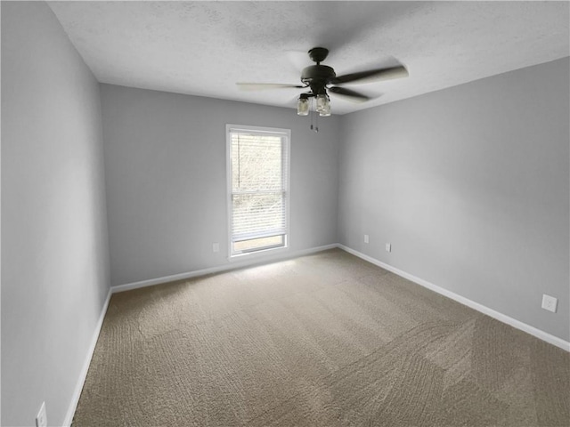 empty room with a textured ceiling, carpet flooring, baseboards, and ceiling fan