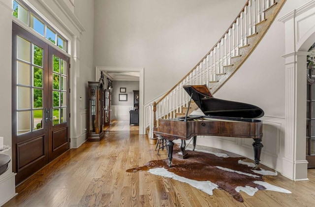 foyer entrance featuring decorative columns, french doors, a towering ceiling, and light wood-type flooring