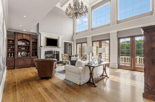 living room featuring french doors, a high ceiling, an inviting chandelier, light hardwood / wood-style flooring, and crown molding