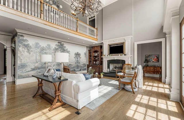 living room with ornate columns, ornamental molding, hardwood / wood-style floors, a chandelier, and a high ceiling