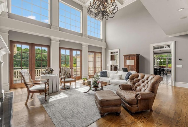 living room featuring ornate columns, a wealth of natural light, french doors, a notable chandelier, and a towering ceiling