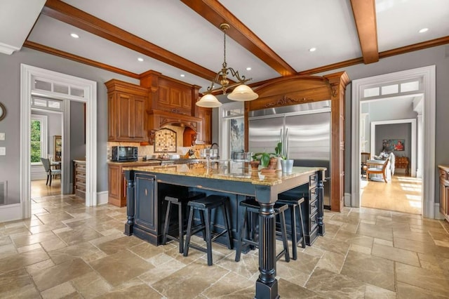 kitchen with light stone countertops, beam ceiling, decorative light fixtures, a center island with sink, and a breakfast bar area