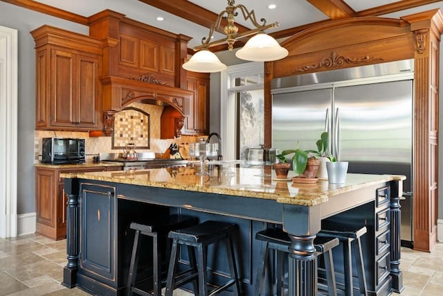 kitchen with light stone countertops, hanging light fixtures, and a kitchen island with sink