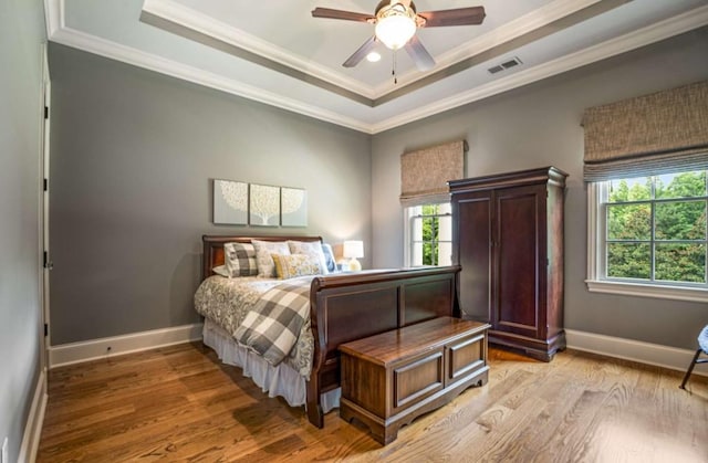 bedroom with light hardwood / wood-style flooring, a raised ceiling, ceiling fan, and ornamental molding