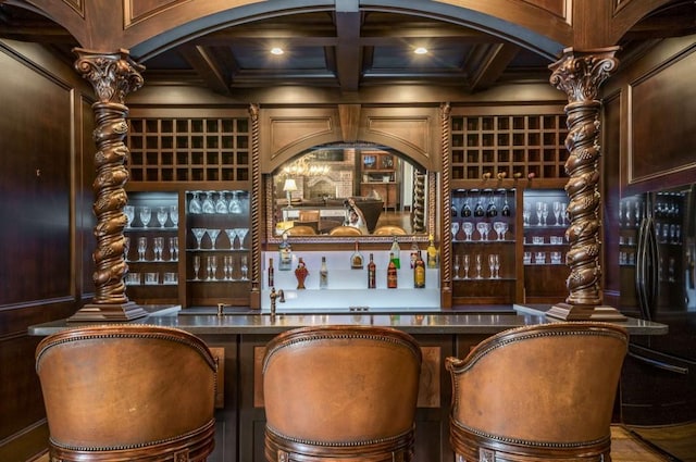 bar featuring coffered ceiling, black fridge, wooden walls, beamed ceiling, and stainless steel counters