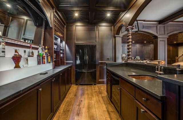 bar featuring black appliances, ornate columns, beamed ceiling, and coffered ceiling