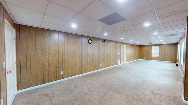 basement featuring a paneled ceiling, wood walls, and carpet floors