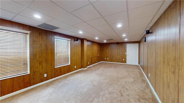 basement featuring a paneled ceiling, wooden walls, and light colored carpet