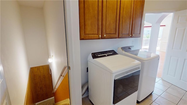 clothes washing area featuring cabinets, light tile patterned floors, and washing machine and clothes dryer