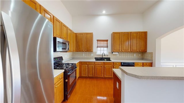 kitchen featuring light wood-type flooring, sink, backsplash, and black appliances