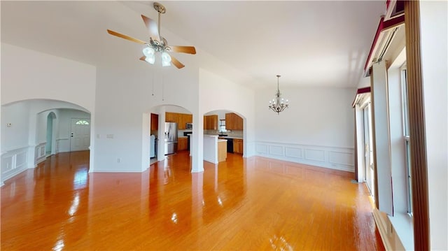 empty room featuring high vaulted ceiling, light hardwood / wood-style floors, and ceiling fan with notable chandelier