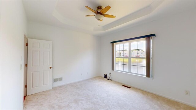 carpeted spare room with a raised ceiling and ceiling fan