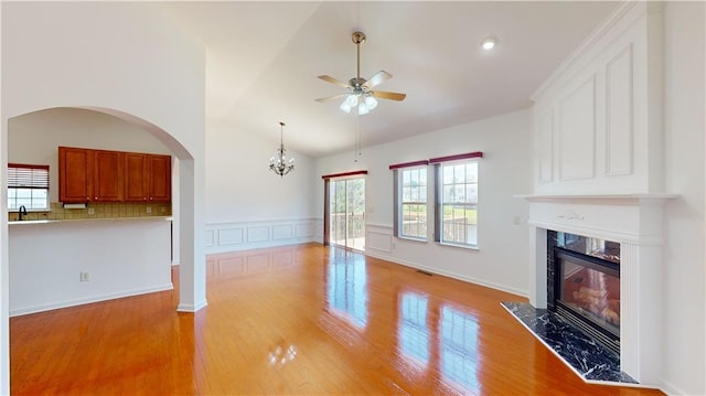 unfurnished living room with a high end fireplace, ceiling fan with notable chandelier, sink, high vaulted ceiling, and light hardwood / wood-style flooring