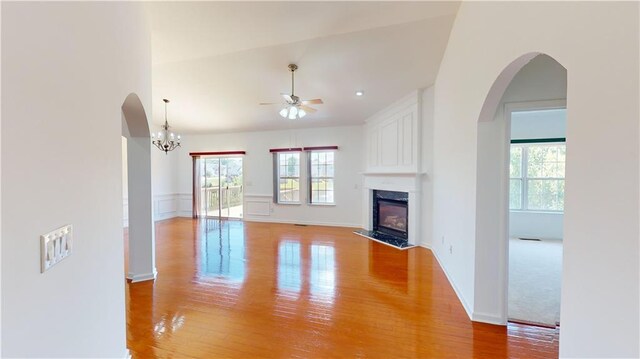 unfurnished living room featuring a high end fireplace, ceiling fan with notable chandelier, and light hardwood / wood-style flooring