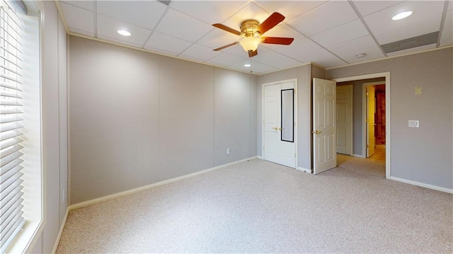 empty room with light colored carpet, a drop ceiling, and ceiling fan