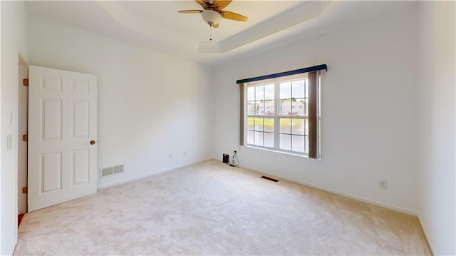 unfurnished room featuring a tray ceiling, light carpet, and ceiling fan