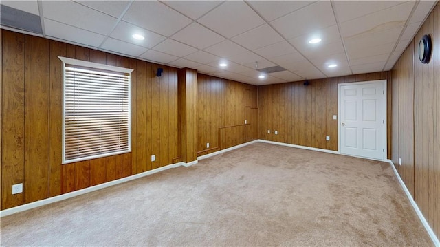 basement with a paneled ceiling, light colored carpet, and wood walls