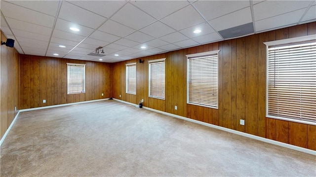 unfurnished room featuring a healthy amount of sunlight, a paneled ceiling, light colored carpet, and wooden walls