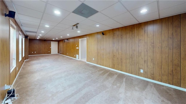 unfurnished room with wooden walls, a drop ceiling, and carpet floors