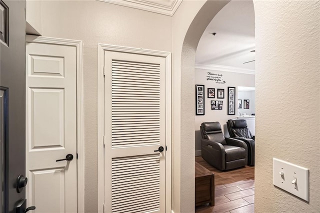 corridor with ornamental molding, a textured wall, arched walkways, and wood finished floors