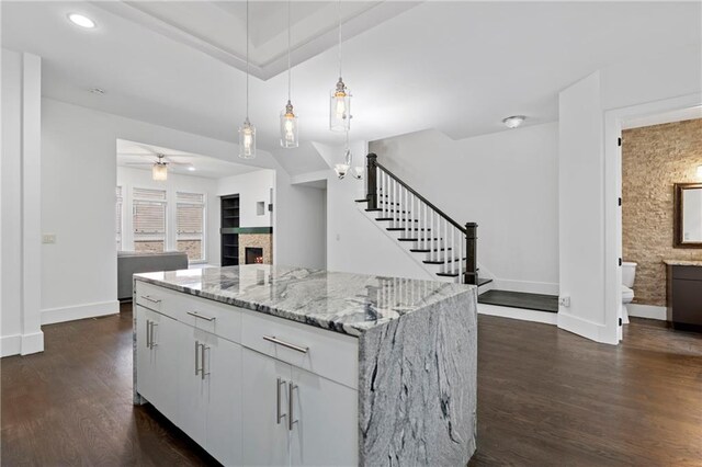 482 Pearl Cove Ct, Atlanta, GA 30350 - kitchen with a lit fireplace, dark wood-style flooring, baseboards, a center island, and light stone counters