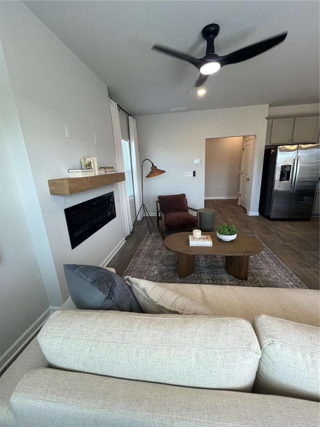 living area with a ceiling fan, a glass covered fireplace, baseboards, and wood finished floors