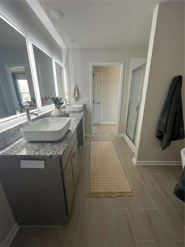 full bathroom featuring baseboards, double vanity, a sink, and a shower stall