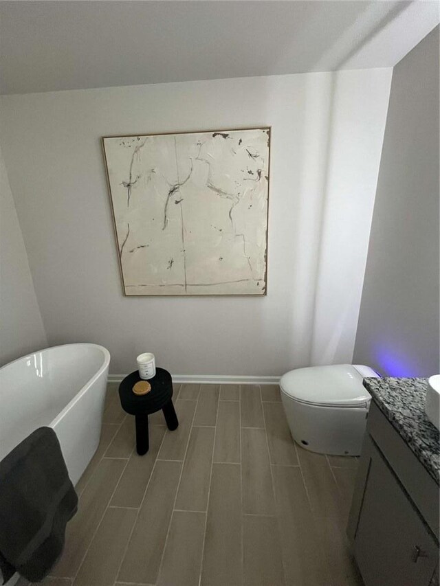 bathroom with baseboards, toilet, vanity, a freestanding bath, and wood finish floors