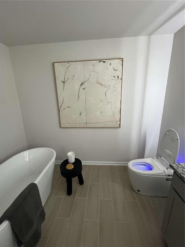 full bath with toilet, baseboards, a freestanding bath, and wood finish floors