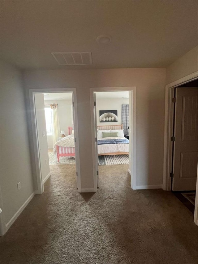 hallway featuring carpet floors, visible vents, and baseboards