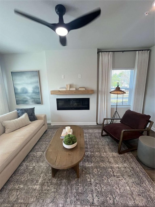 living area featuring ceiling fan, wood finished floors, a glass covered fireplace, and baseboards