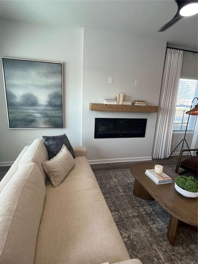 living area with wood finished floors, a glass covered fireplace, a ceiling fan, and baseboards