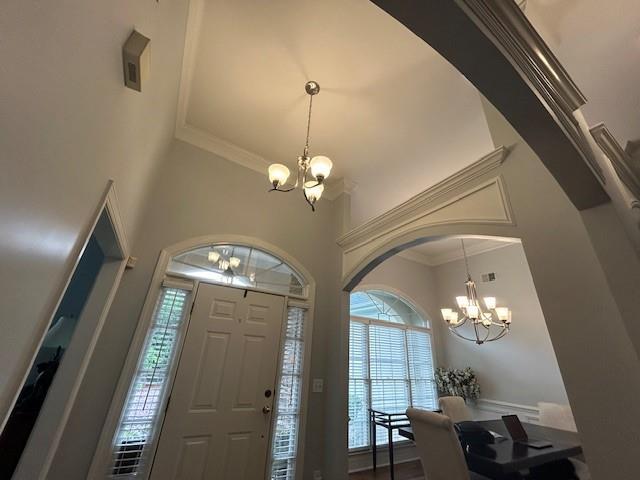 entrance foyer with crown molding, arched walkways, a high ceiling, and a chandelier