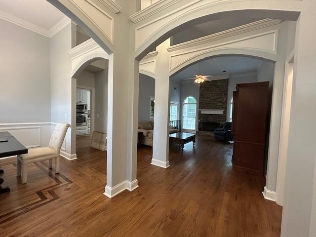 corridor with ornamental molding, arched walkways, and wood finished floors