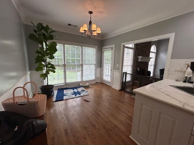 interior space with visible vents, crown molding, a fireplace, dark wood-style floors, and a chandelier