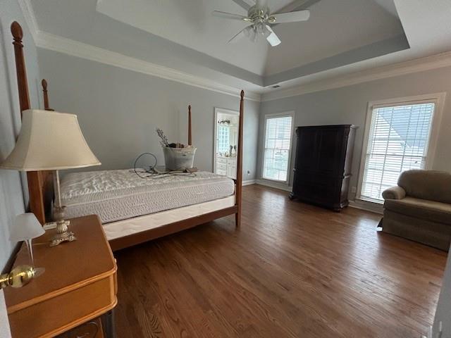 bedroom with ceiling fan, a raised ceiling, baseboards, wood finished floors, and ornamental molding