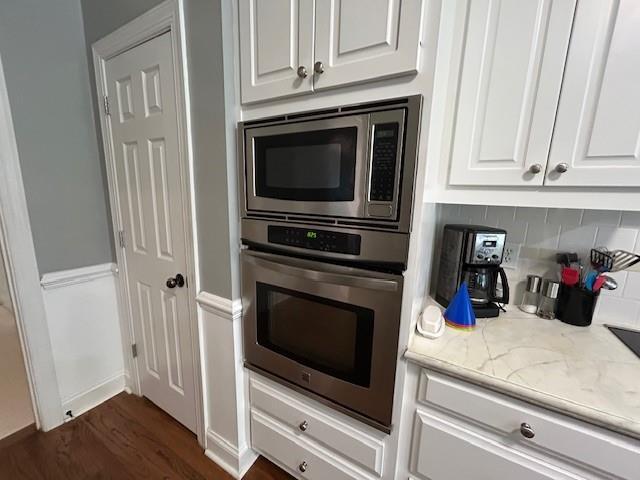 kitchen with white cabinets, light stone countertops, dark wood finished floors, stainless steel appliances, and tasteful backsplash