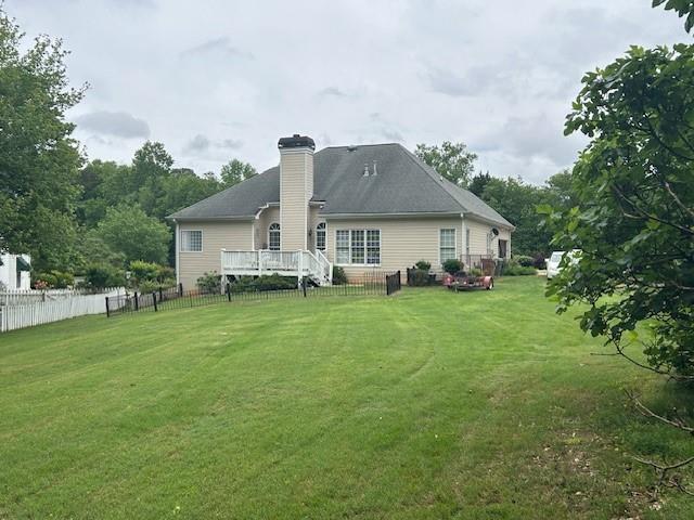 rear view of house featuring fence, a wooden deck, a chimney, and a lawn