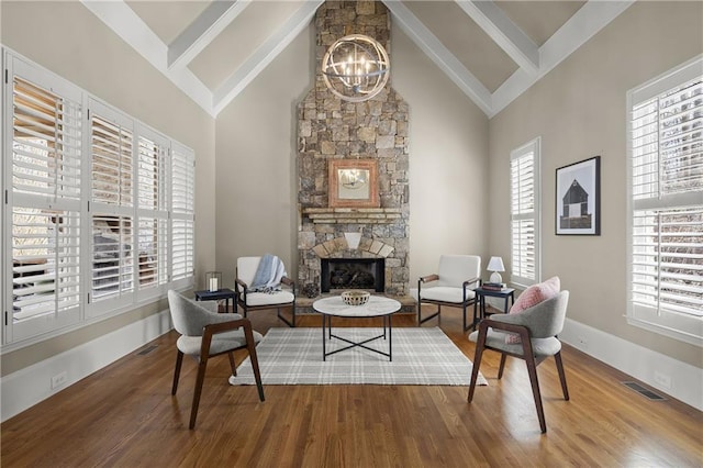 sitting room with visible vents, a chandelier, wood finished floors, a stone fireplace, and high vaulted ceiling