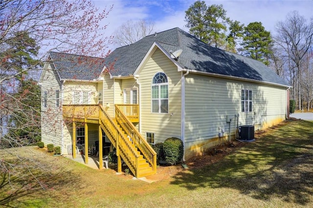 rear view of house featuring cooling unit, roof with shingles, a wooden deck, a yard, and stairs