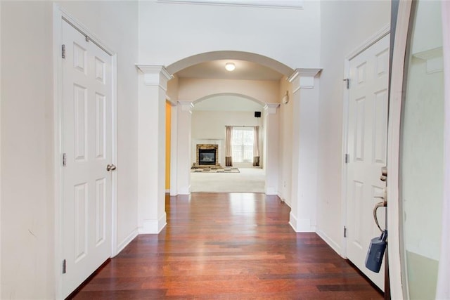 hallway featuring decorative columns, wood finished floors, baseboards, and arched walkways