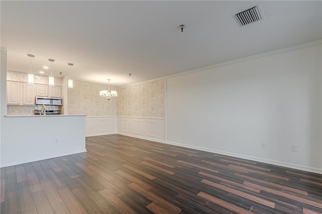 unfurnished living room featuring dark hardwood / wood-style floors, an inviting chandelier, and ornamental molding