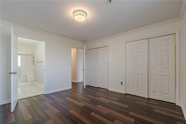 unfurnished bedroom with two closets, connected bathroom, dark hardwood / wood-style floors, and crown molding